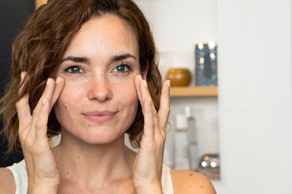 Mature woman touching cheeks looking in bathroom mirror