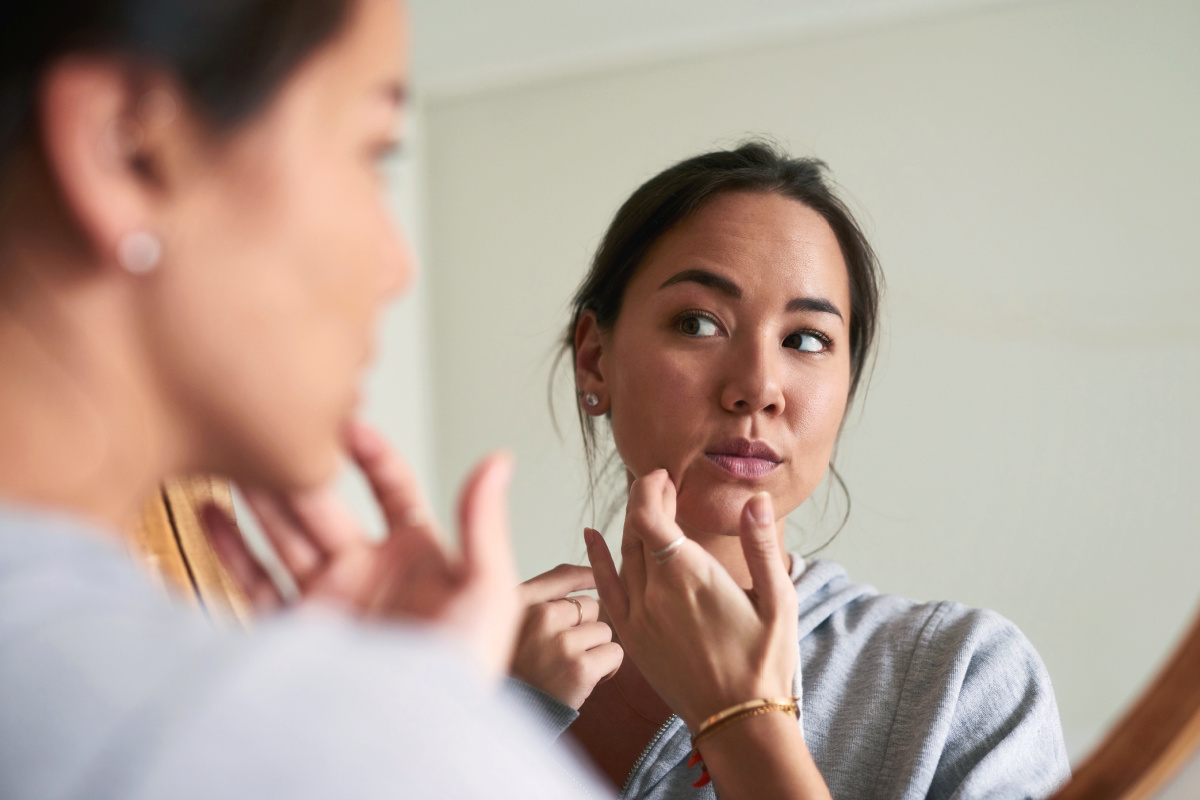 Asian woman looking in mirror at skin with concern