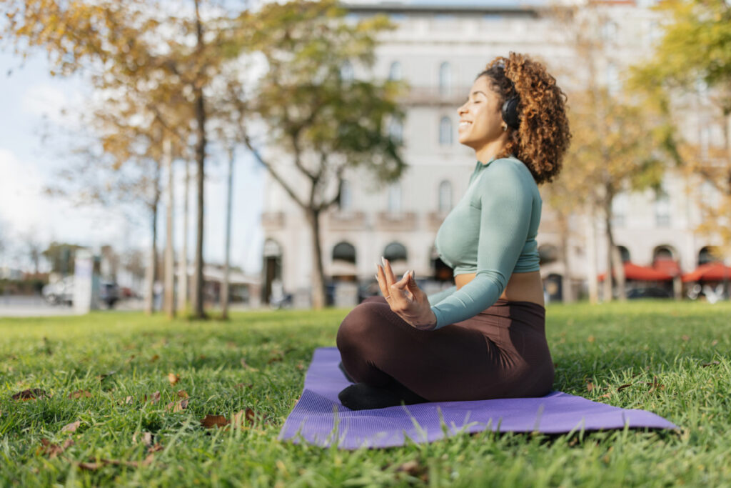 Woman smiling while meditating outside on purple yoga mat for mental wellness